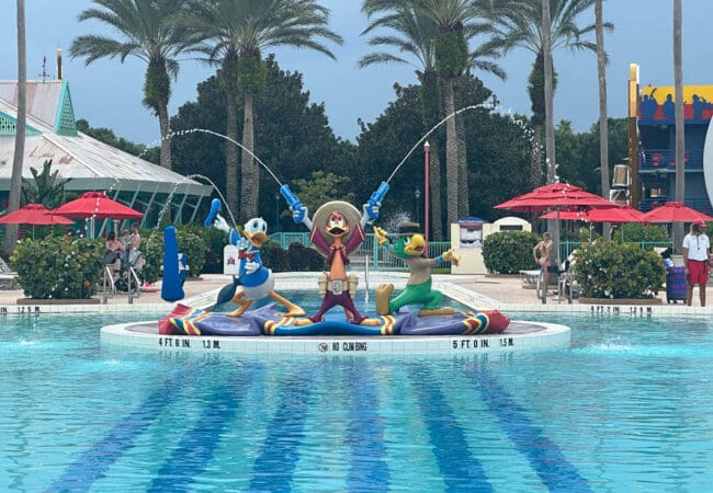 Donald Duck, José Carioca en Panchito op zwembad fontein in Disney resort met palmbomen en parasols