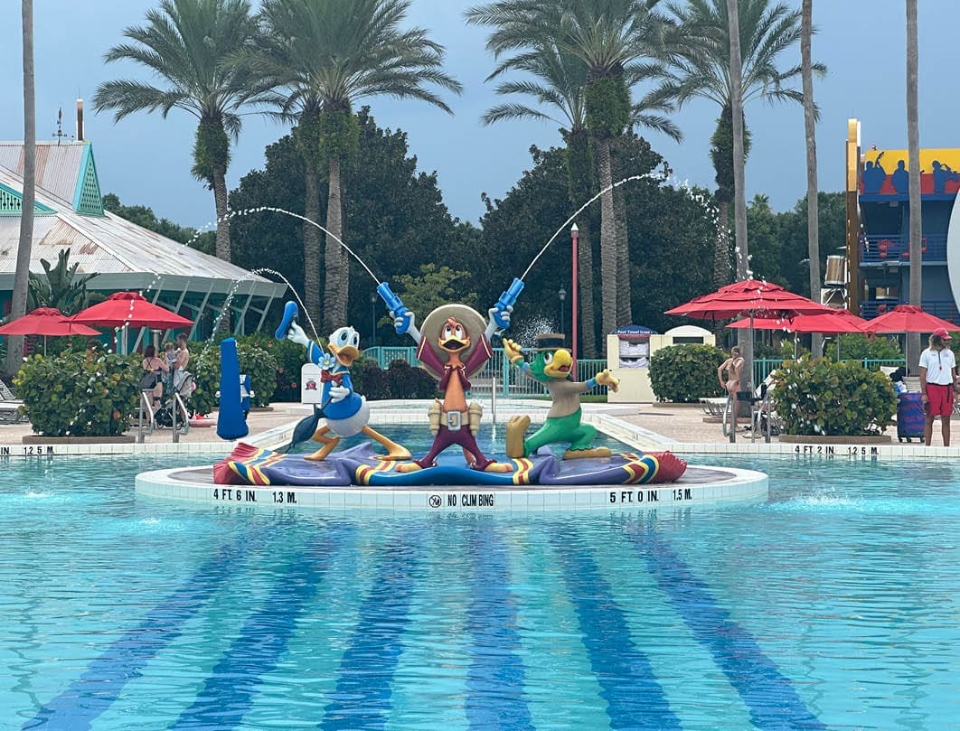 Donald Duck, José Carioca en Panchito op zwembad fontein in Disney resort met palmbomen en parasols