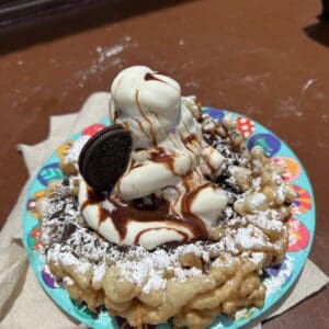 Funnel cake beladen met vanille-ijs, chocoladesaus, Oreo-koekje en poedersuiker op een Disney-bordje